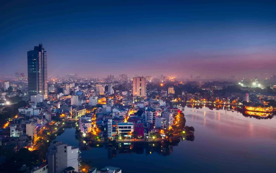 Vue nocturne de Hanoi : reflets dorés sur le lac, buildings modernes et ruelles animées, entre tradition vietnamienne et effervescence urbaine.