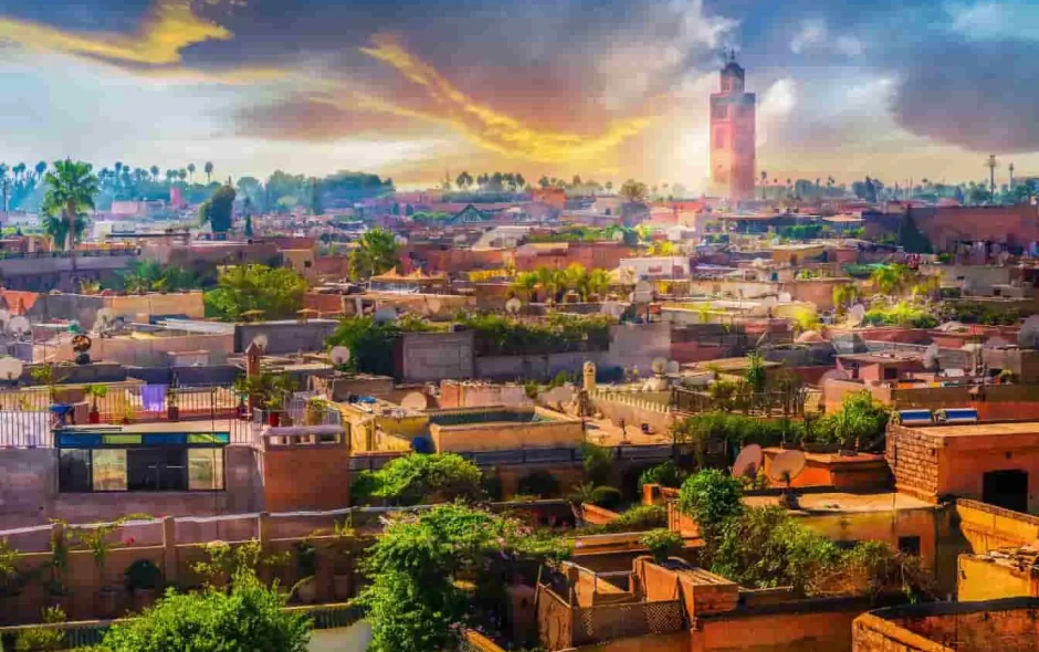 Coucher de soleil sur Marrakech, Maroc : minaret de la Koutoubia, palmiers et toits ocres baignent dans une lumière dorée et vibrante.