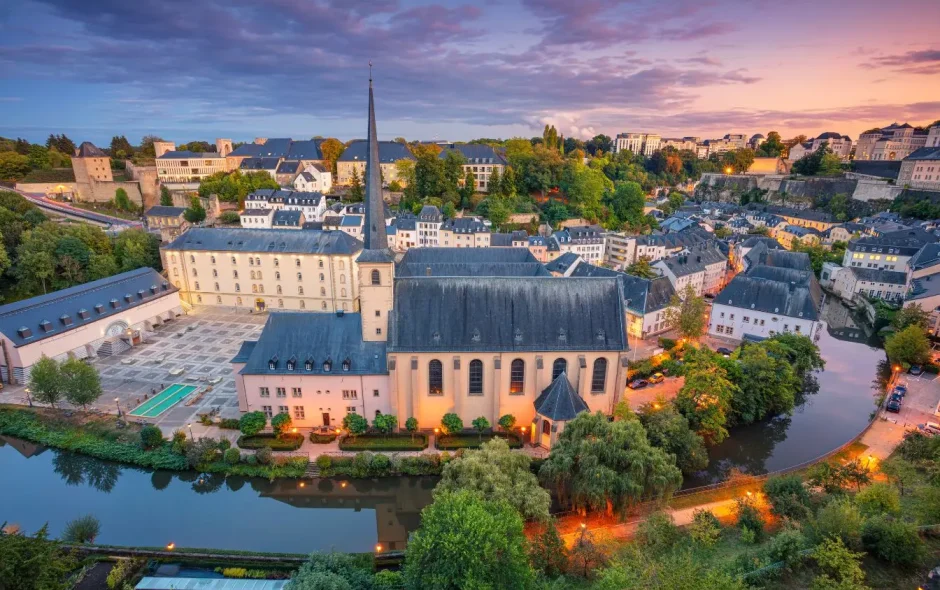 Vue au coucher du soleil sur l’abbaye de Neumünster bordée par la rivière, image évoquant le charme de Luxembourg