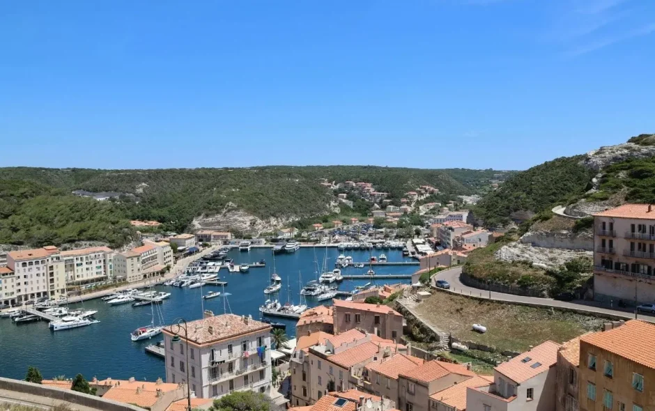 Vue sur marina bordée de toits ocres et collines verdoyantes illustrant le charme méditerranéen de Bonifacio