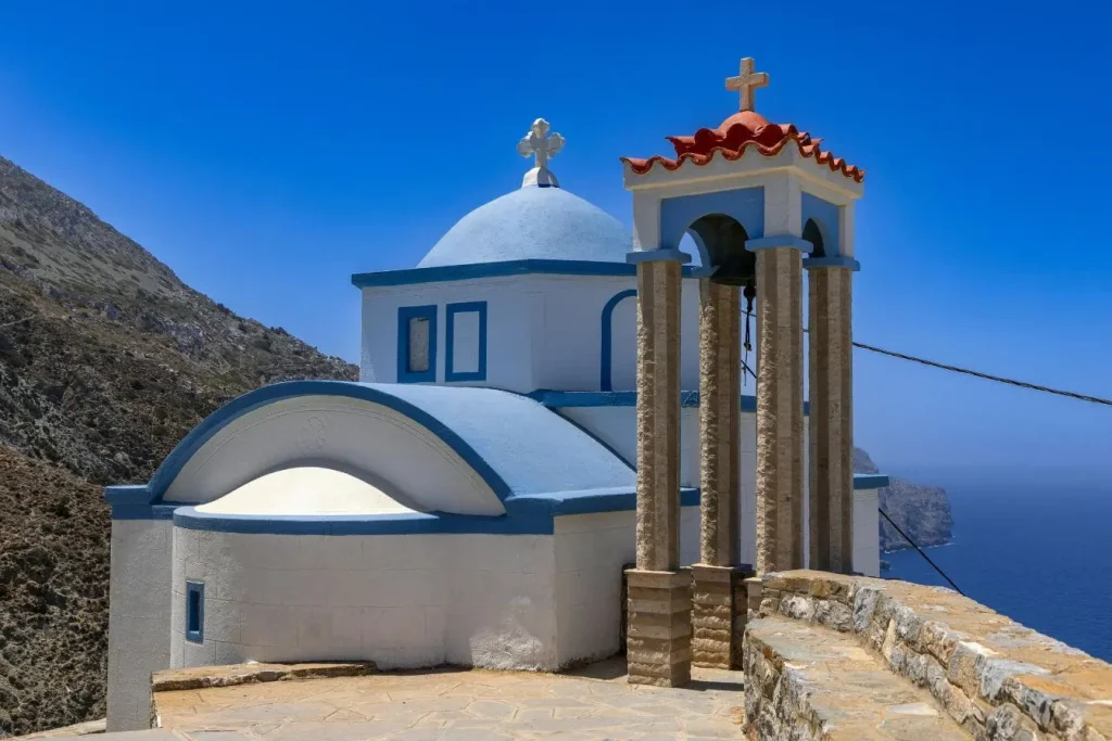Église orthodoxe blanche au dôme bleu dominant la mer, image reflétant les traditions de Pâques en Grèce et la ferveur religieuse des célébrations