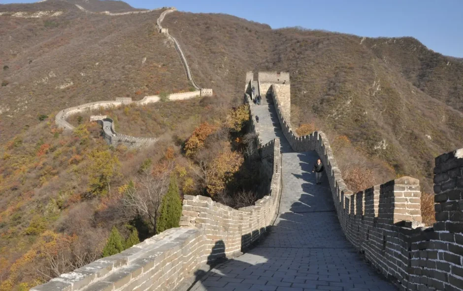 Vue aérienne de la Grande Muraille serpentant sur montagnes colorées d’automne, image illustrant la majesté et l’histoire de ce monument emblématique.