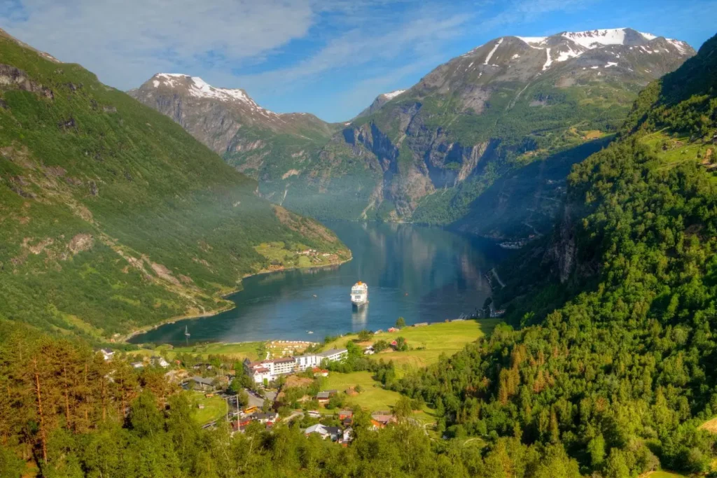 Croisière majestueuse au cœur d’un fjord norvégien entouré de montagnes verdoyantes et sommets enneigés, image illustrant la beauté naturelle du pays.