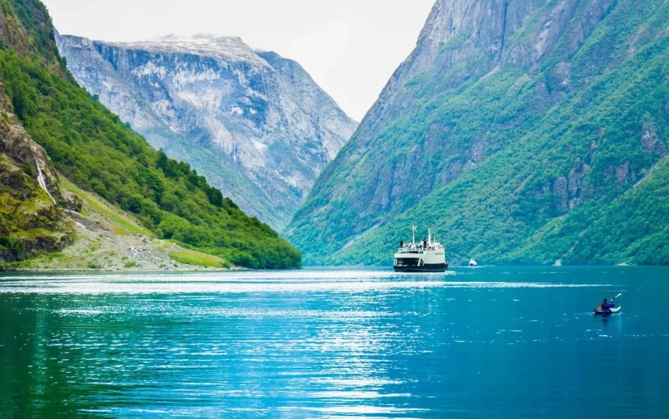 Ferry avançant sur eau calme entourée de montagnes verdoyantes, image illustrant la beauté majestueuse des fjords de Norvège.