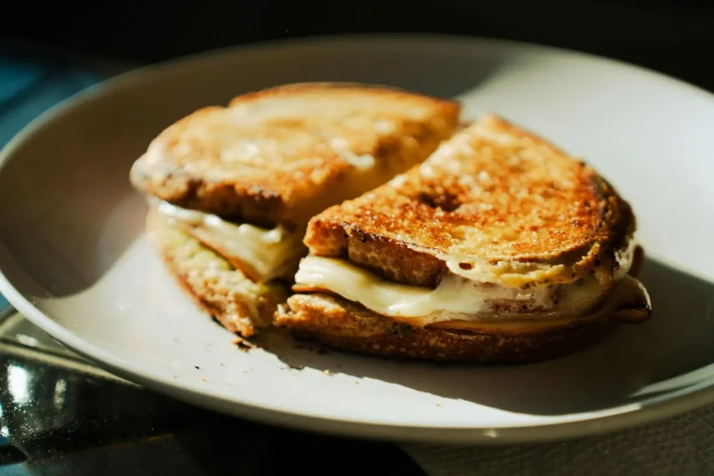 Sandwich grillé doré coupé en deux sur assiette blanche reflétant authenticité des spécialités savoyardes et convivialité des repas montagnards