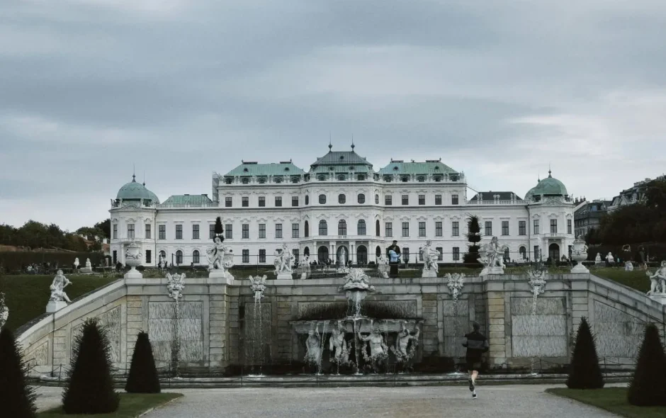 Vue du palais baroque de Vienne avec dômes verts et fontaine ornée de statues, image illustrant l’élégance architecturale et culturelle autrichienne.