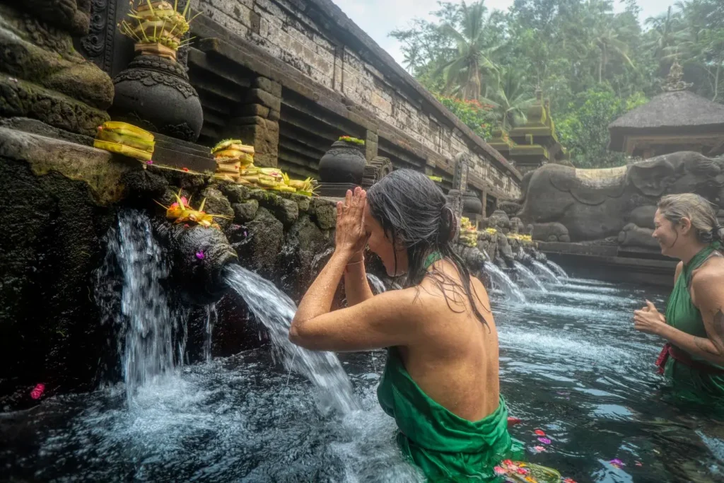 Personnes en prière sous un jet d’eau, image représentant les traditions religieuses en Thaïlande et la quête de pureté.