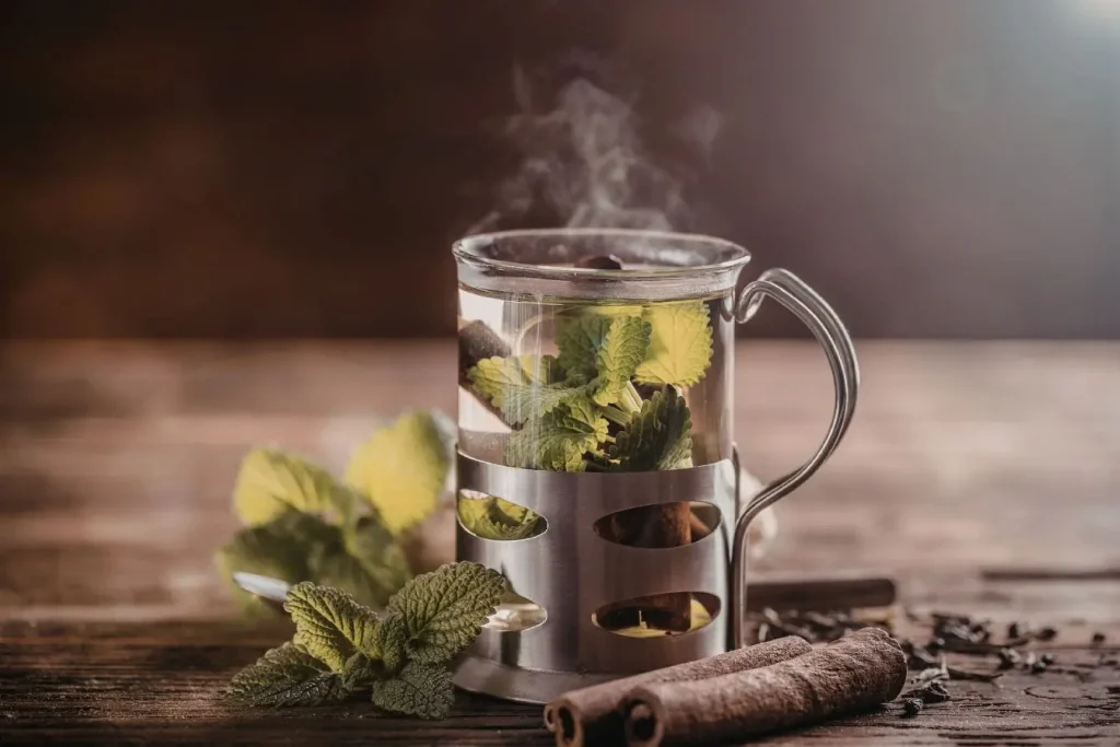 Verre de thé fumant avec menthe et cannelle sur bois, image illustrant le rituel du thé à la menthe dans la culture berbère au Maroc.
