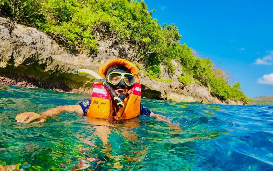 Personne en gilet orange explore les eaux turquoise près d’une côte verdoyante illustrant une expérience de snorkeling aux Maldives.