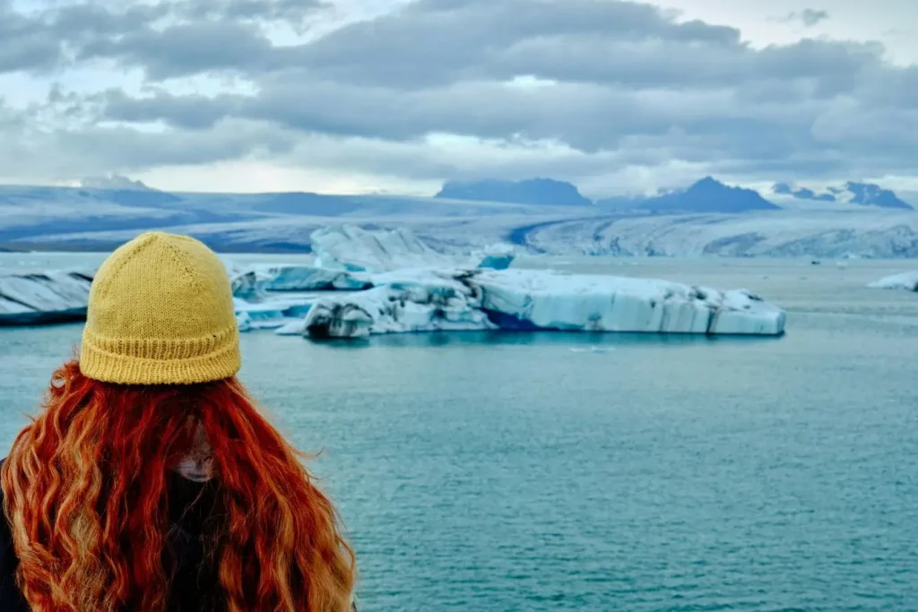 Personne au bonnet jaune observant lagune glacée avec icebergs et montagnes enneigées reflétant beauté sauvage et authenticité d’un voyage en Islande