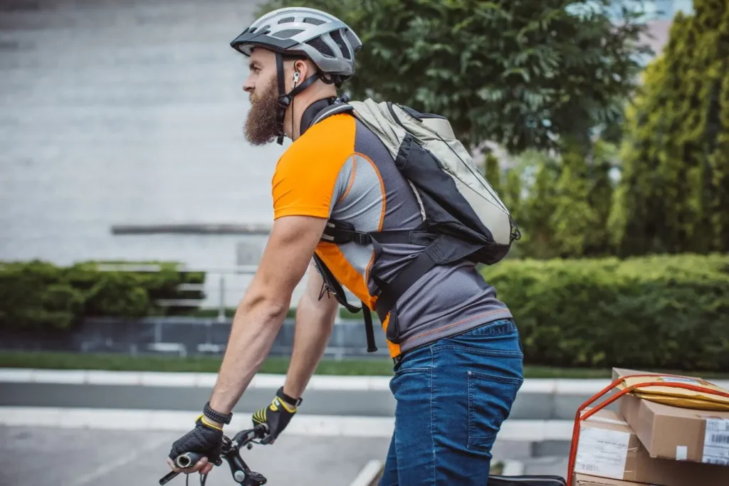 Cycliste en tenue orange et sac à dos pédale avec colis sur vélo, image représentant les transports en Nouvelle-Zélande