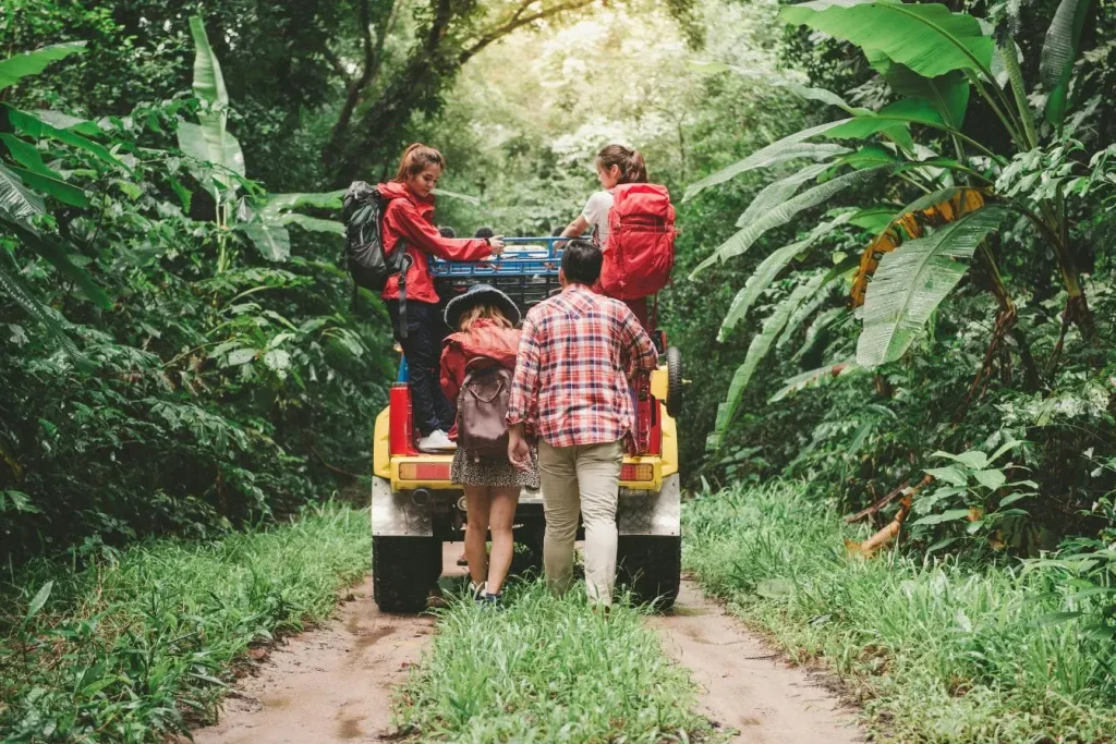 Groupe de voyageurs debout derrière véhicule jaune sur chemin forestier, image illustrant un voyage éco-responsable privilégiant la découverte en pleine nature.
