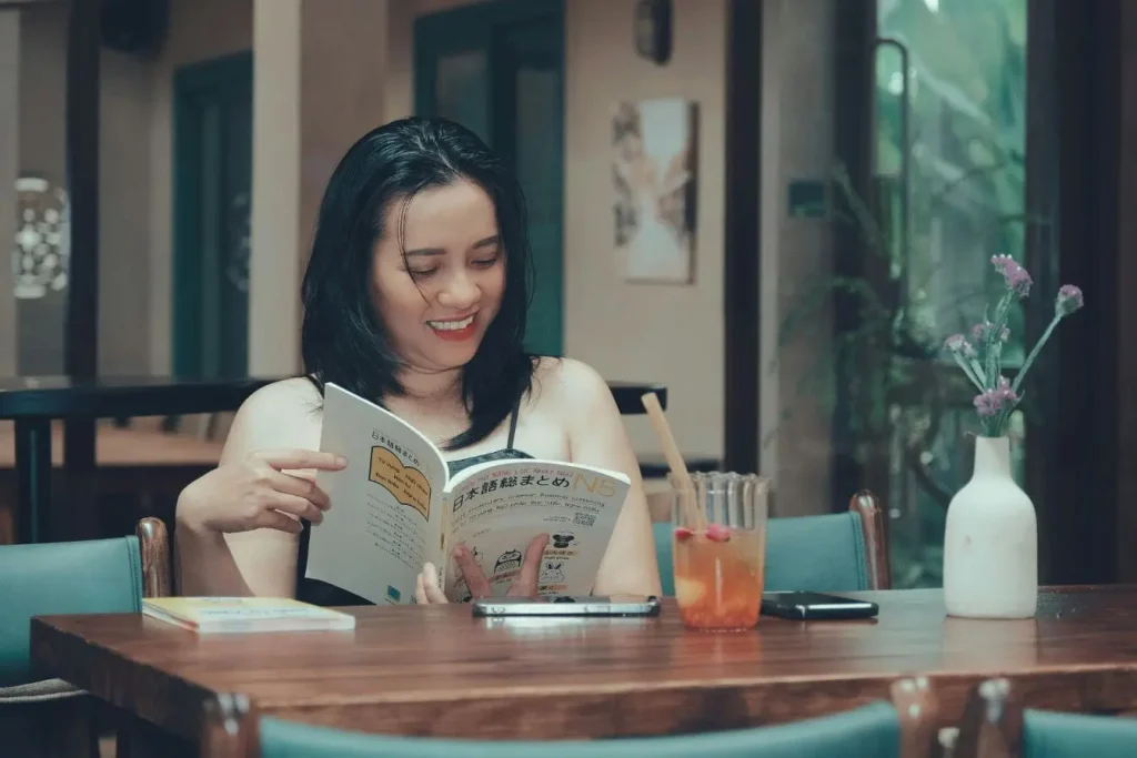 Personne lisant manuel de japonais N5 sur table, image illustrant l’importance d’apprendre le vocabulaire de base d’une langue avant de voyager.