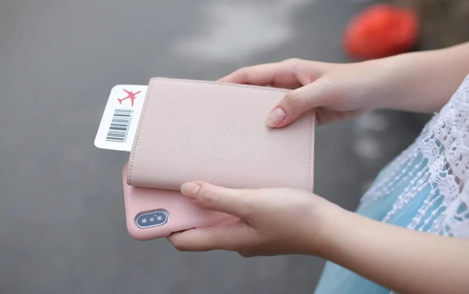 Mains tenant passeport rose et smartphone assorti avec billet visible, image illustrant la recherche du meilleur moment pour réserver un vol au prix idéal.