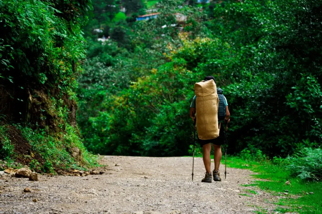 Randonneur avançant sur sentier forestier avec grand sac, image illustrant un voyage éco-responsable privilégiant la marche et la nature.