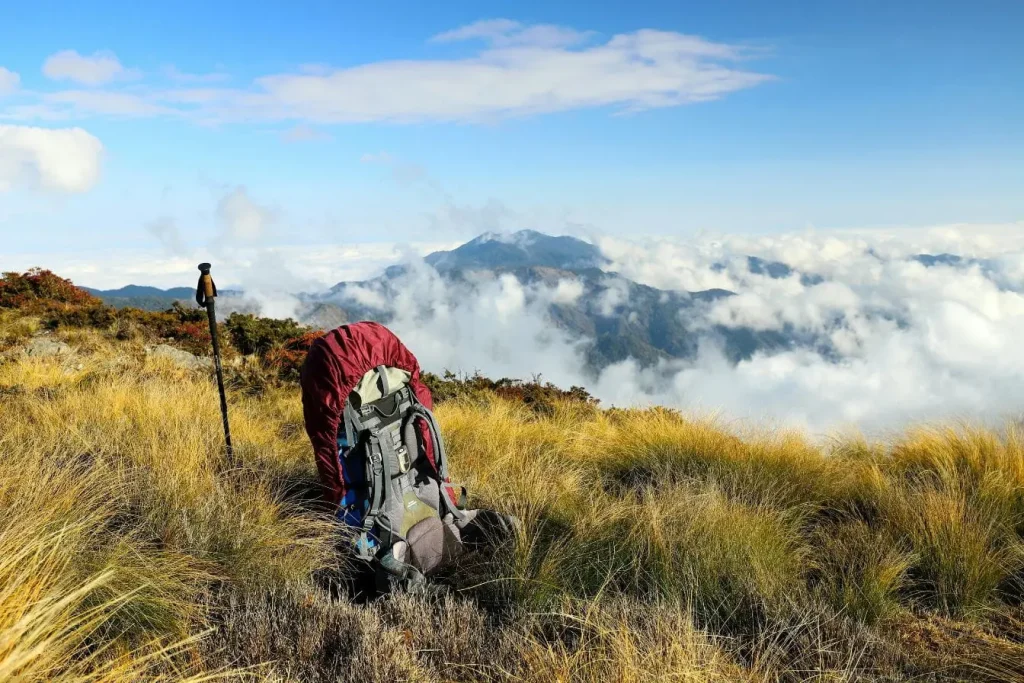 Grand sac de randonnée et bâton plantés dans l’herbe, symbole de l’aventure et des défis d’un trek en altitude.