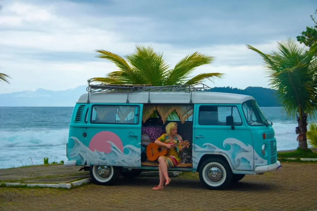 Van turquoise et blanc décoré de vagues garé près de la plage, image illustrant le voyage en van aménagé et la liberté de vivre en bord de mer.