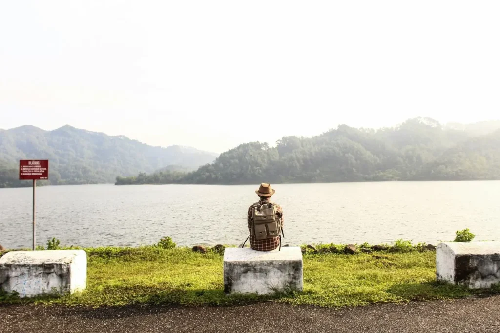 Personne assise sur un bloc de béton face à un lac, image évoquant un voyage avec un très petit budget en profitant simplement de la nature.