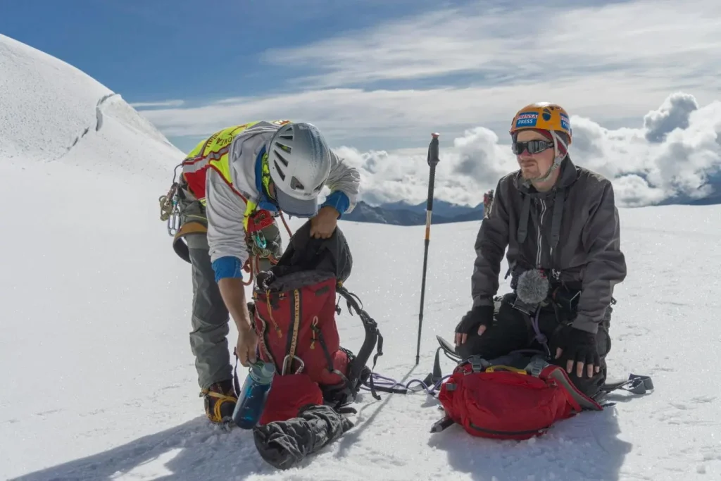 Deux alpinistes équipés de casques et cordes sur pente enneigée, image illustrant la préparation et l’effort d’un trek en altitude.