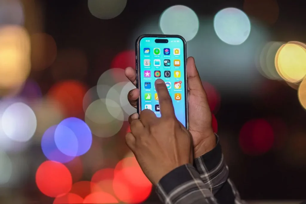 Gros plan sur smartphone tenu à deux mains affichant icônes colorées, image illustrant l’usage d’une application de voyage pour explorer et organiser trajets.