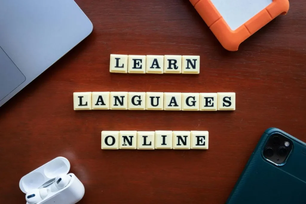 Lettres formant learn languages online sur table avec objets tech, image illustrant l’importance d’apprendre le vocabulaire de base avant de voyager.