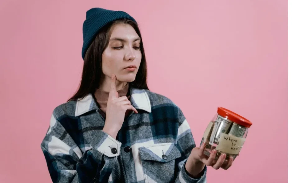 Personne tenant un bocal rempli de billets roulés, image évoquant l’idée de voyager avec un très petit budget en économisant chaque dollar.