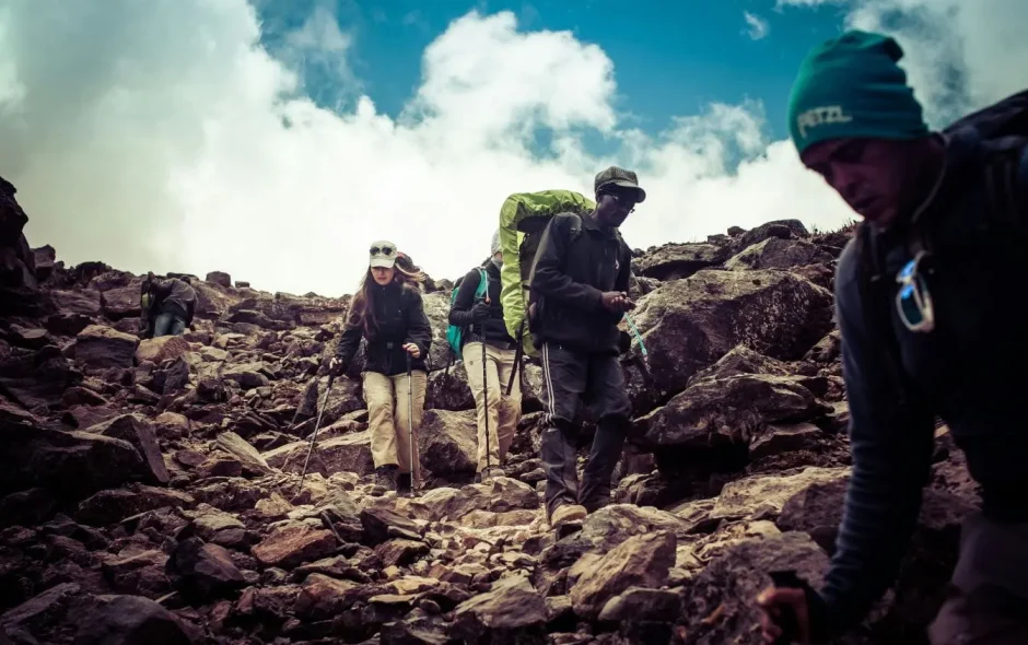 Groupe de randonneurs descendant un sentier rocheux en montagne, image illustrant l’effort physique et l’aventure d’un trek en altitude.