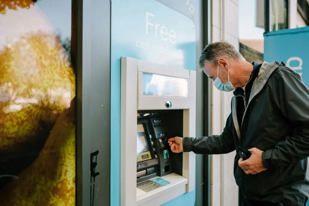Personne masquée utilisant distributeur automatique extérieur, image illustrant la meilleure banque sans frais pour voyager à l’étranger.