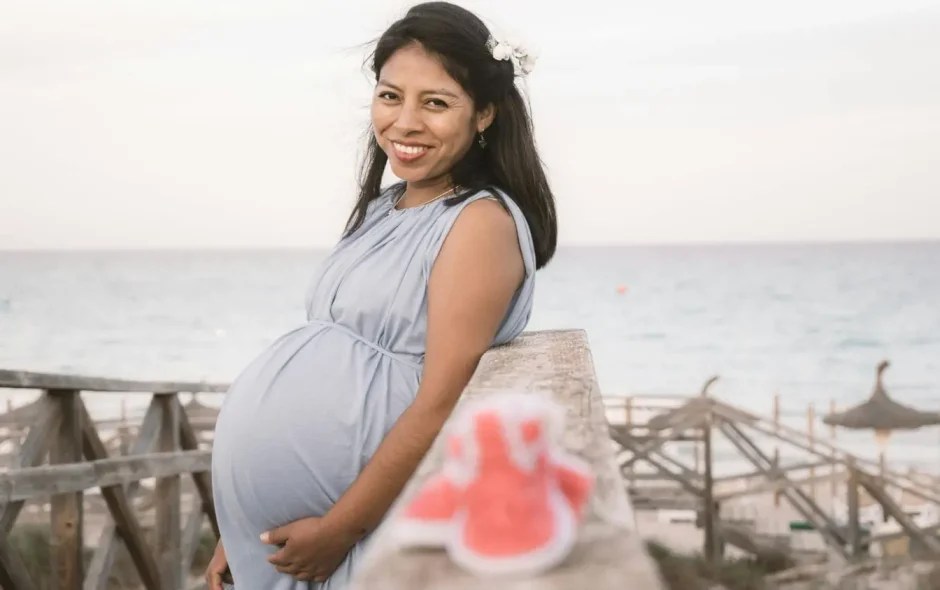 Femme enceinte en robe bleue près de la mer reflétant la sérénité et les précautions nécessaires pour voyager enceinte en toute sécurité.