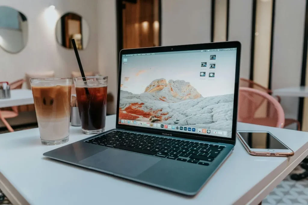MacBook Air posé sur table de café moderne avec boissons glacées, image illustrant travailler en voyageant en tant que freelance et la flexibilité numérique.
