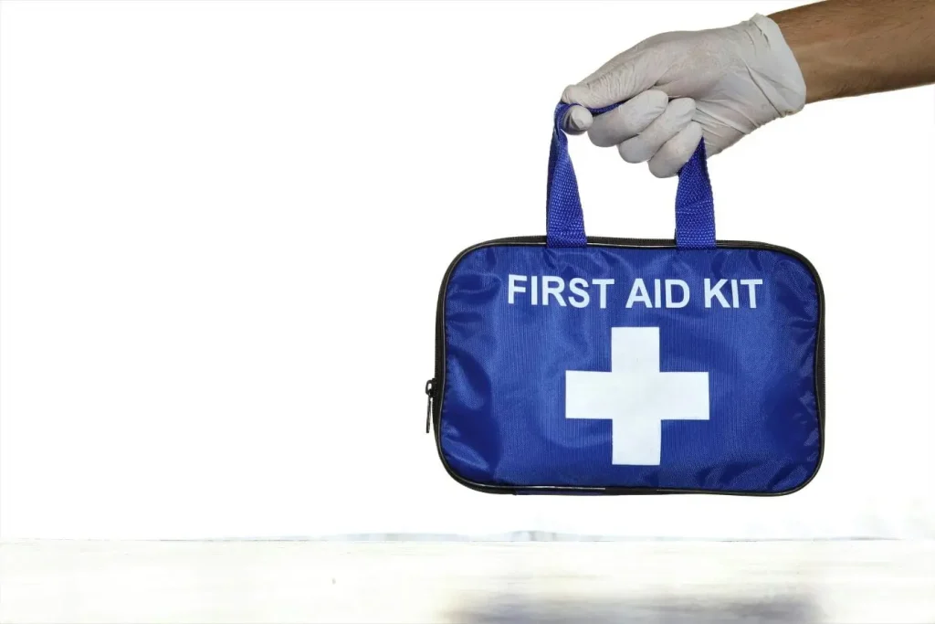 Sac bleu avec croix blanche tenu par main gantée, illustrant la trousse à pharmacie de voyage indispensable pour les déplacements.
