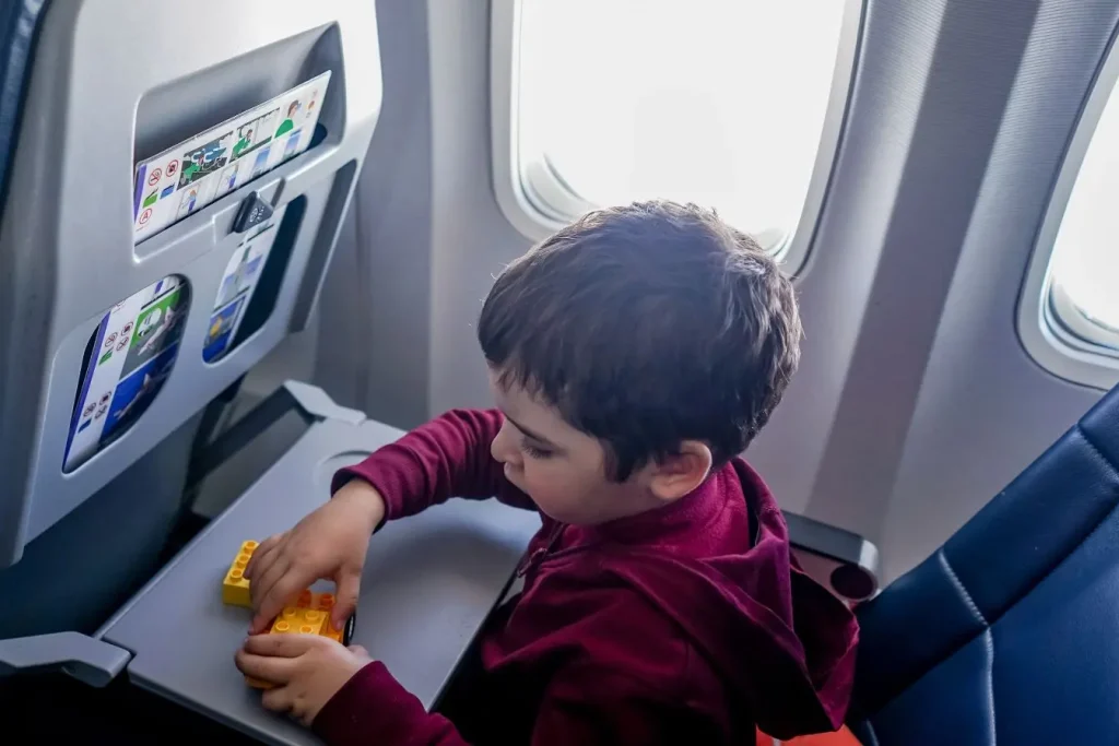 Enfant assis près du hublot jouant avec blocs, image illustrant l’importance de rester occupé pour éviter le mal des transports en avion.