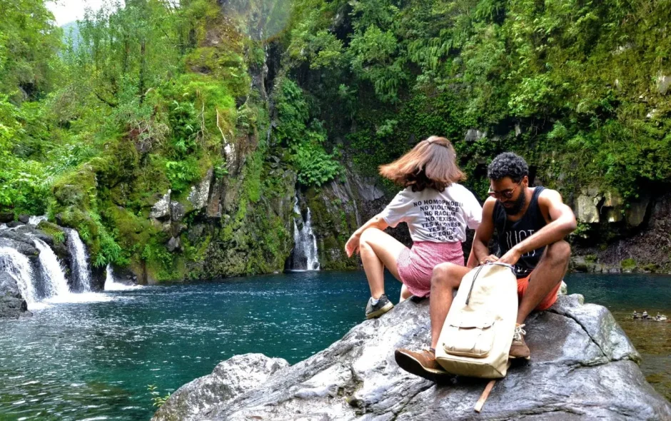 Deux personnes assises près d’une cascade dans la forêt, moment paisible qui illustre un voyage respectueux de la nature et durable.