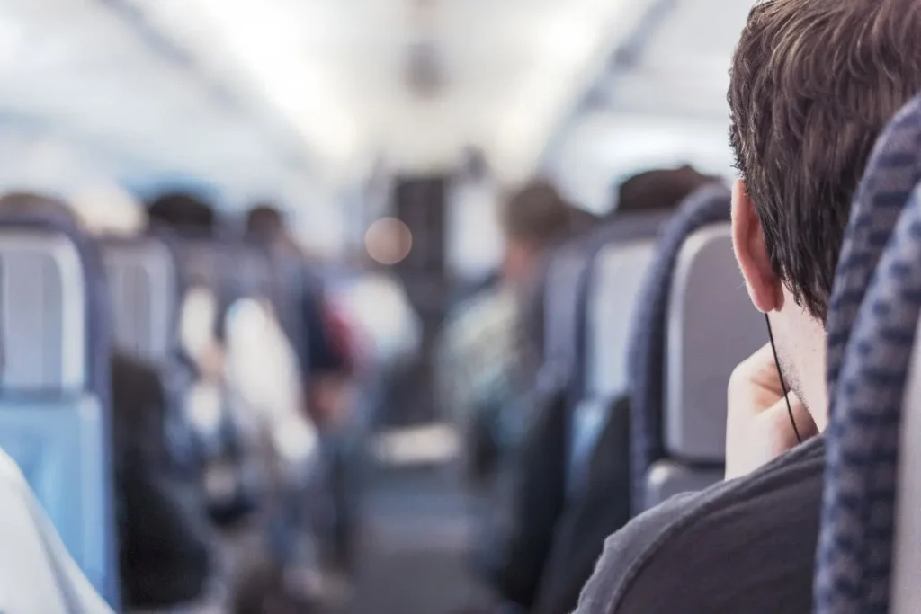 Passager assis avec écouteurs dans une cabine d’avion montrant l’importance de créer un environnement calme pour bien dormir en vol.