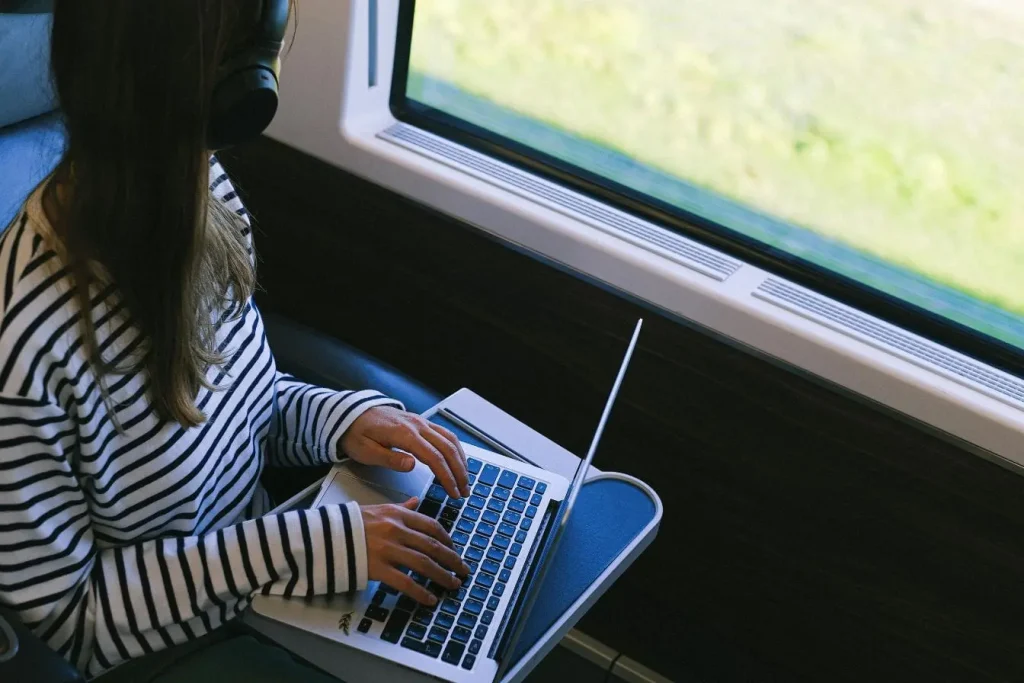 Voyageur portant casque et chemise rayée utilisant ordinateur, image représentant travailler en voyageant en tant que freelance et la flexibilité numérique.