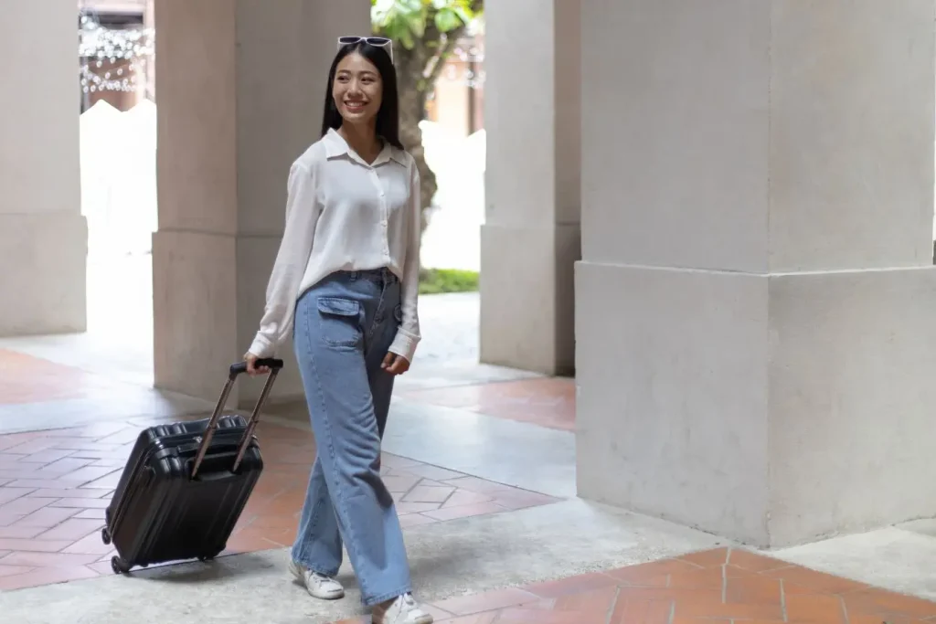 Voyageur en chemise blanche et jeans tirant petite valise noire à roulettes dans couloir lumineux, image illustrant la meilleure valise cabine pour voyager souvent.