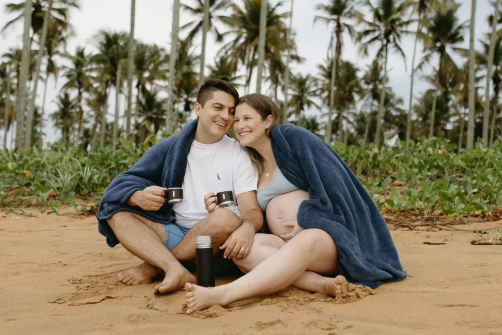 Deux personnes assises sur sable sous couverture bleue reflétant la sérénité et les précautions nécessaires pour voyager enceinte en toute tranquillité.