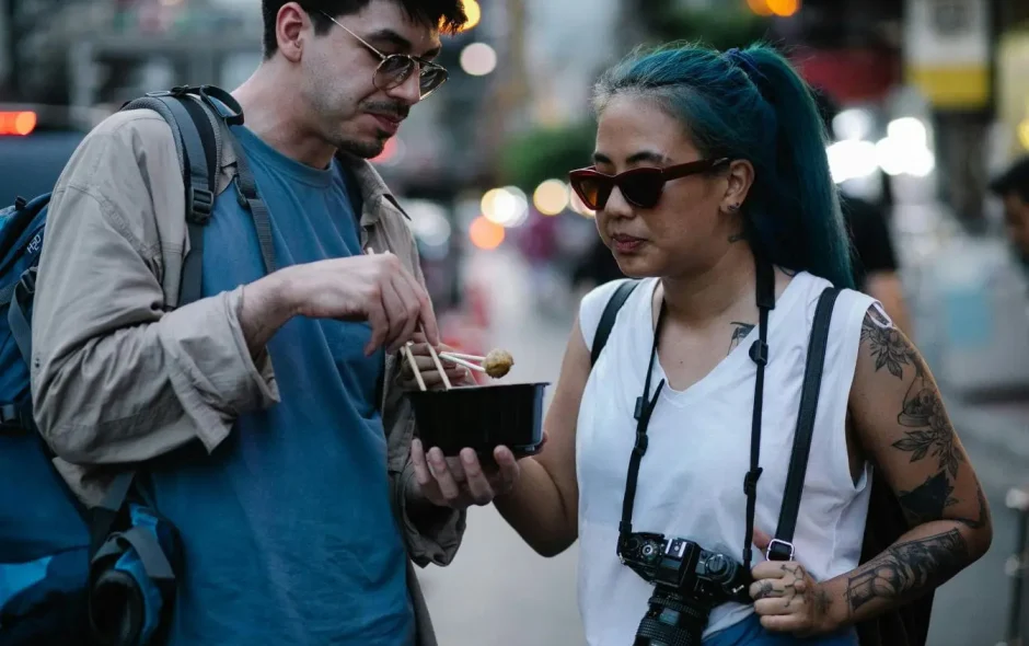 Personnes partageant un bol de nourriture dans une rue animée, représentant la vigilance nécessaire pour éviter la tourista en voyage.