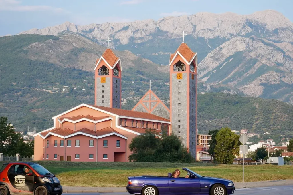 Église moderne aux tours élancées devant montagnes verdoyantes, image qui illustre l’expérience de visiter Tirana en Albanie.
