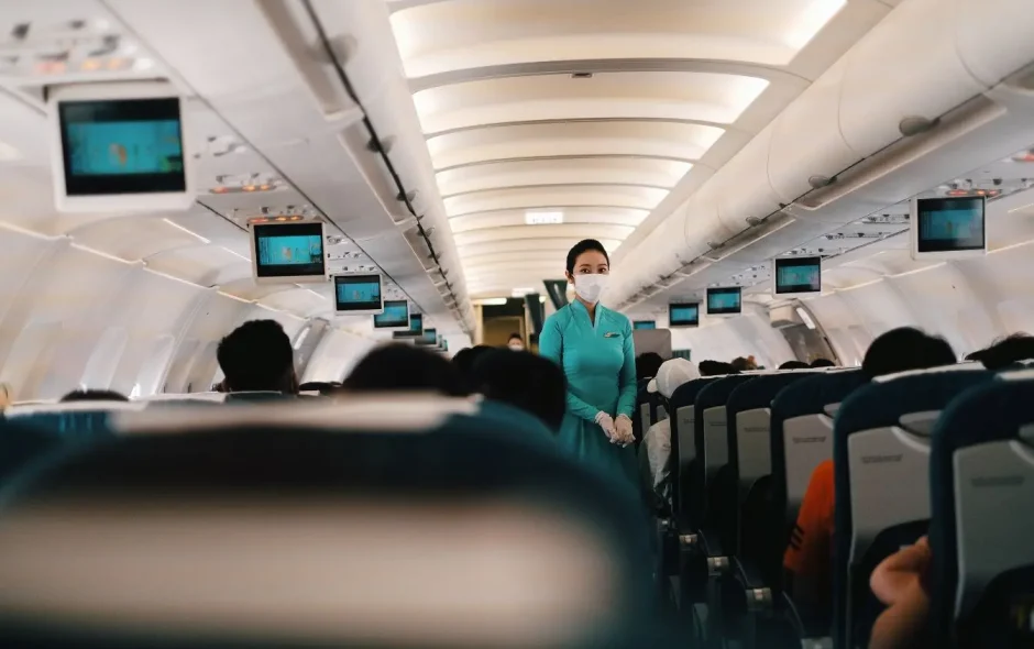 Cabine d’avion remplie de passagers avec hôtesse masquée, image illustrant la situation d’un vol retardé et les droits des voyageurs.