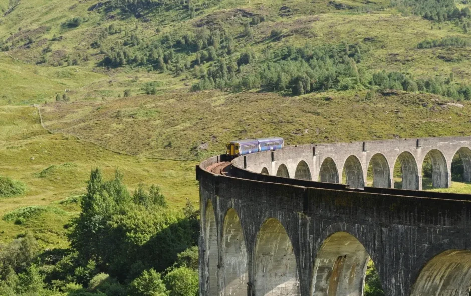 Train bleu traversant un viaduc de pierre au milieu d’une vallée verdoyante, image qui illustre la beauté des paysages autour d’Inverness.