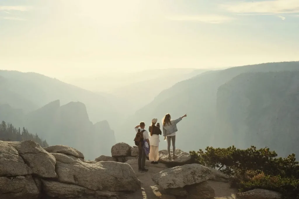 Trois personnes debout sur falaise rocheuse admirent montagnes embrumées, image illustrant la beauté de visiter la Cappadoce.