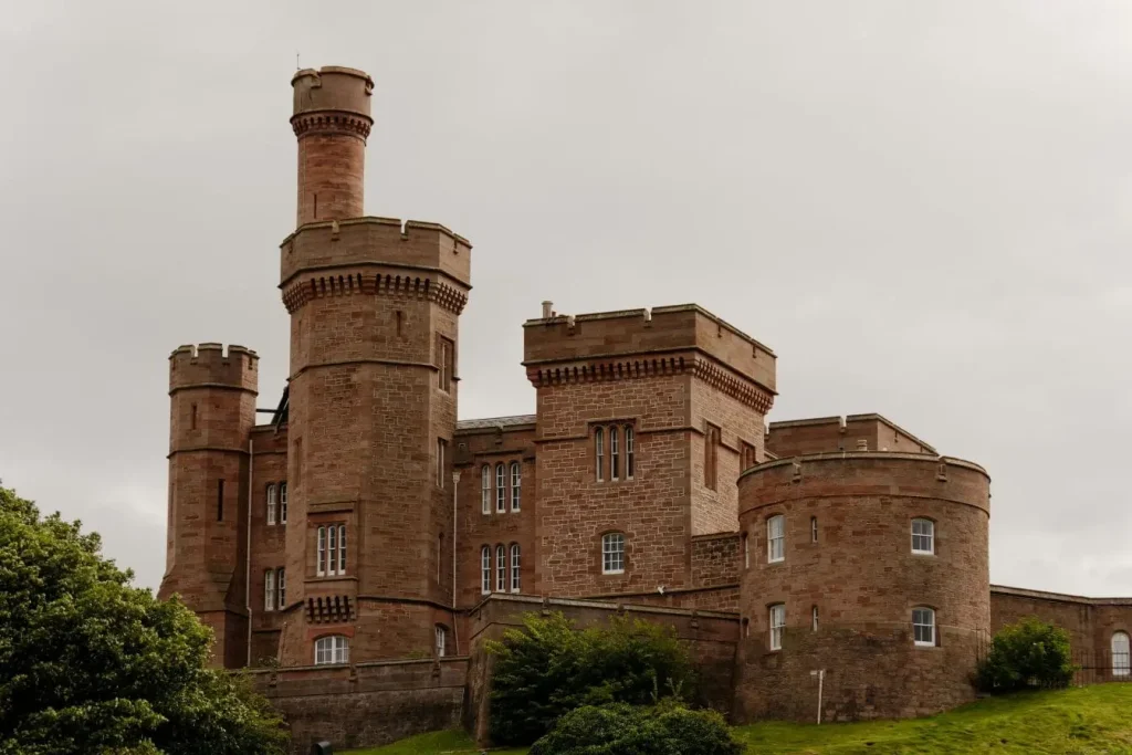 Château de pierre rougeâtre aux tours imposantes sur colline verdoyante, image qui illustre le charme historique d’Inverness dans les Highlands.