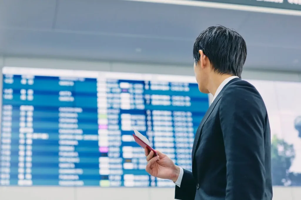 Voyageur en costume consulte grand écran d’aéroport, image illustrant la vérification des vols retardés et les droits des passagers.