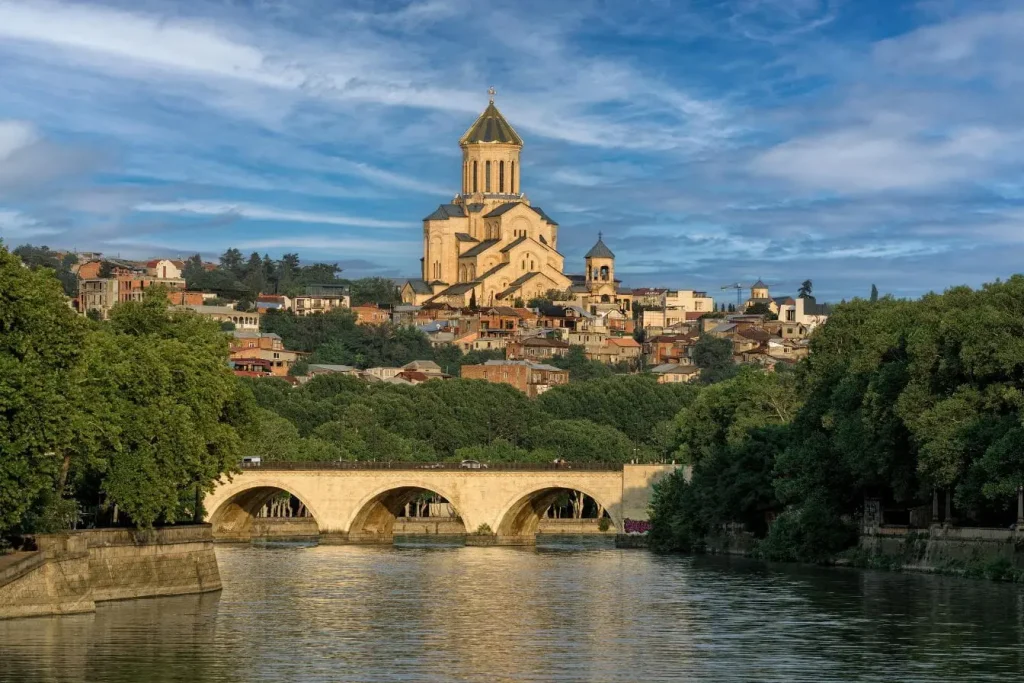 Vue panoramique sur cathédrale dorée entourée de verdure et habitations, symbole de la capitale géorgienne Tbilissi.