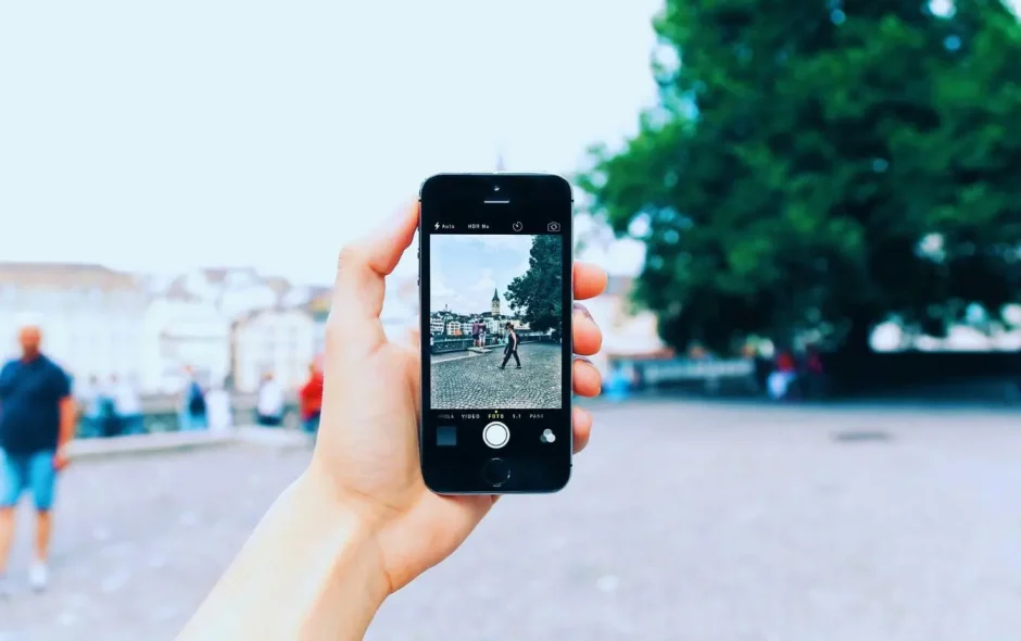 Main tenant smartphone capturant place pavée avec passants, image illustrant la prise de belles photos de voyage avec téléphone.