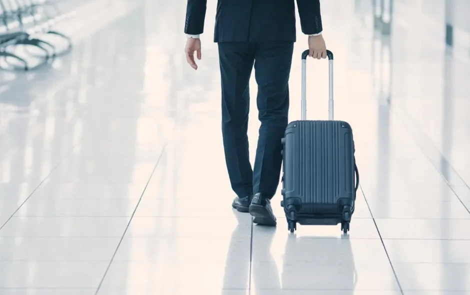 Voyageur en costume tire valise noire dans terminal, image illustrant la préparation pour éviter les frais de surcharge bagages en avion.