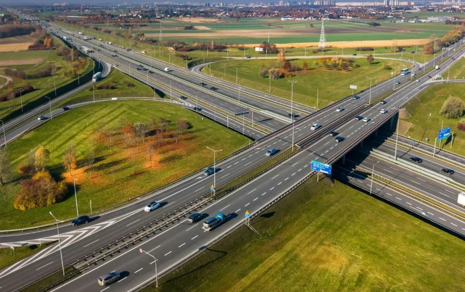 Vue aérienne d’un vaste échangeur routier entouré de verdure et bâtiments au loin, reflet des infrastructures reliant Poznań et ses incontournables.