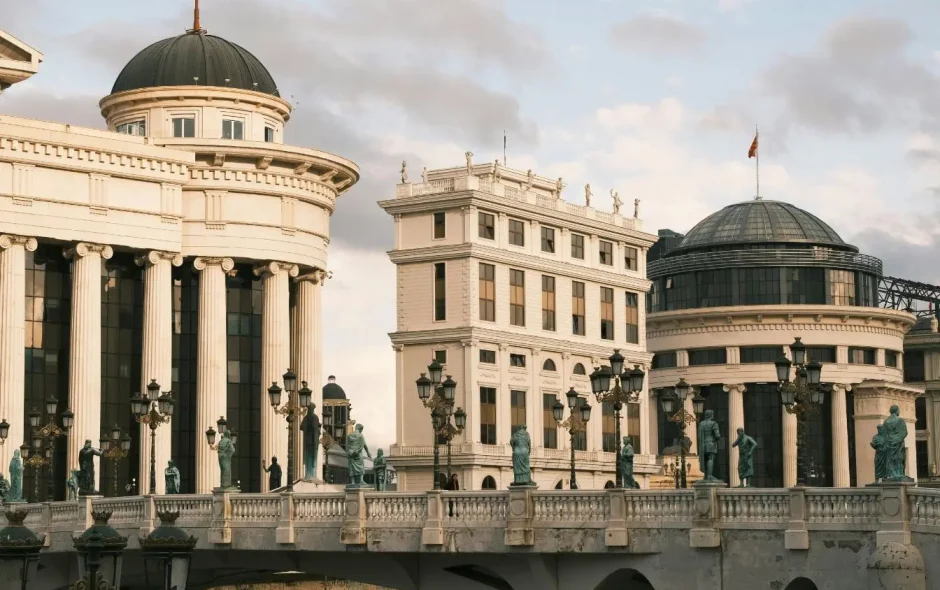 Vue sur pont orné de statues et lampadaires menant à bâtiments néoclassiques, image qui illustre l’expérience unique de visiter Skopje.
