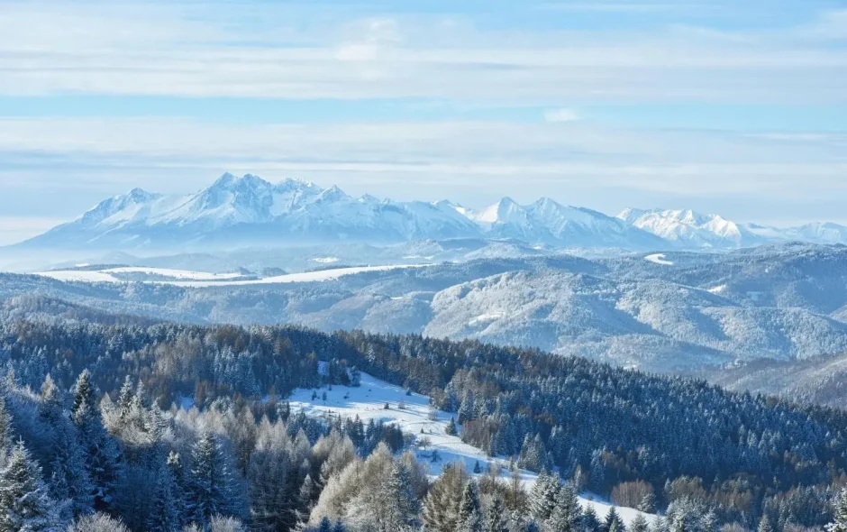 Paysage hivernal avec sommets enneigés et collines boisées, reflet des aventures possibles dans les Tatras slovaques.